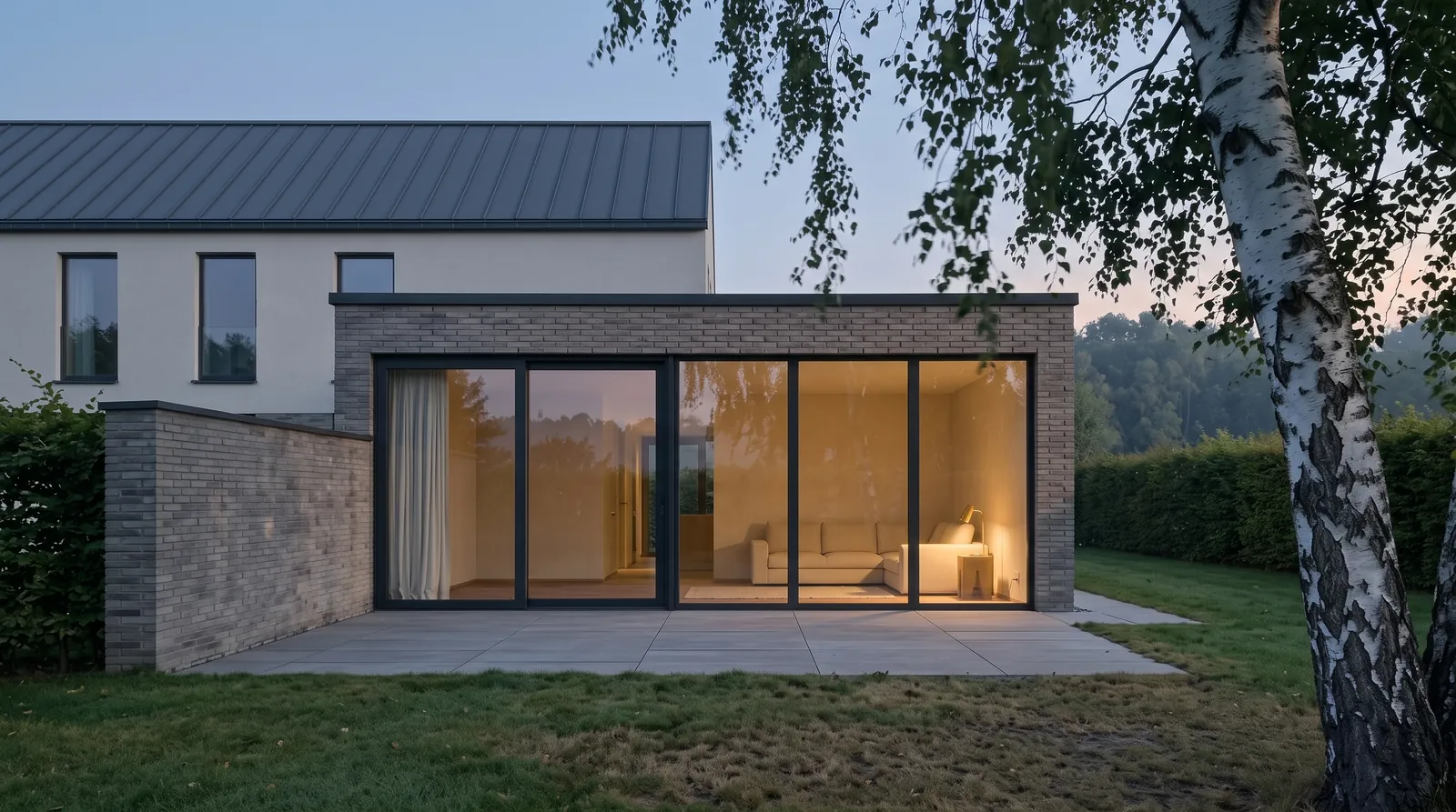 Die Gartenfassade zur blauen Stunde, warmes Licht hinter den Glasfeldern